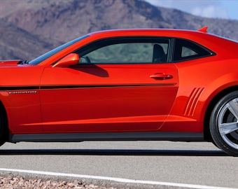 May include: A bright orange sports car with black racing stripes, black wheels, and a black interior. The car is parked on a paved road with a mountain range in the background.