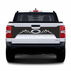 Może przedstawiać: Biały samochód dostawczy Ford Maverick z czarną klapą bagażnika. Klapa bagażnika ma czarną grafikę gór z napisem "Maverick" białymi literami pod górami.