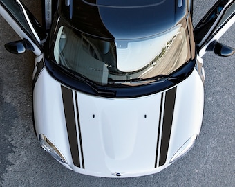May include: A white Mini Cooper S with black racing stripes on the hood. The car has a black roof and the doors are open.