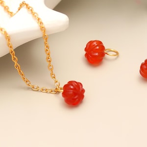 May include: A gold chain necklace with a red, carved pendant, and two matching red earrings. The earrings have gold hoops. The jewelry is set against a light background with a white dish and green sprigs.