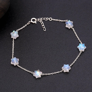 Op de afbeelding: Een delicate zilveren armband met zes stervormige edelstenen. De edelstenen hebben een parelmoerachtige, iriserende kwaliteit, met hints van blauw en wit. De armband is verbonden door een fijne zilveren ketting en heeft een verstelbare sluiting.