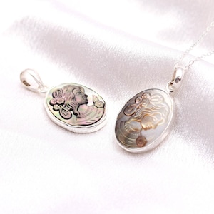 May include: Two oval pendants featuring carved mother-of-pearl cameos of a profile figure with floral hair accents, set in silver-toned metal frames. One pendant is attached to a delicate silver-toned chain, while the other is separate.