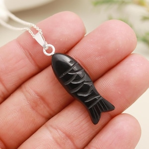 May include: A black onyx fish pendant necklace with a silver chain. The fish is carved with detailed scales and has a smooth, polished finish.