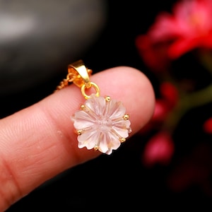 以下が含まれることがあります： 彫刻されたデザインが施された透明なクォーツの花を特徴とする繊細なゴールドペンダント。ペンダントはゴールドチェーンに付いています。