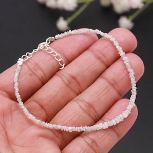 May include: A delicate bracelet featuring small, irregularly shaped, light-colored gemstones strung together. The bracelet has a silver-toned chain and clasp. The gemstones are arranged in a single strand, creating a subtle, elegant accessory.