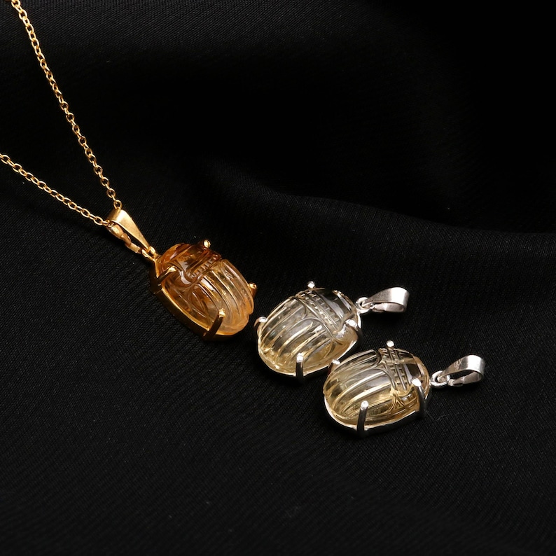 May include: Three scarab beetle pendant necklaces. One pendant is gold-toned with a gold chain, and the other two are silver-toned. The pendants are carved with intricate details and have a light amber color.