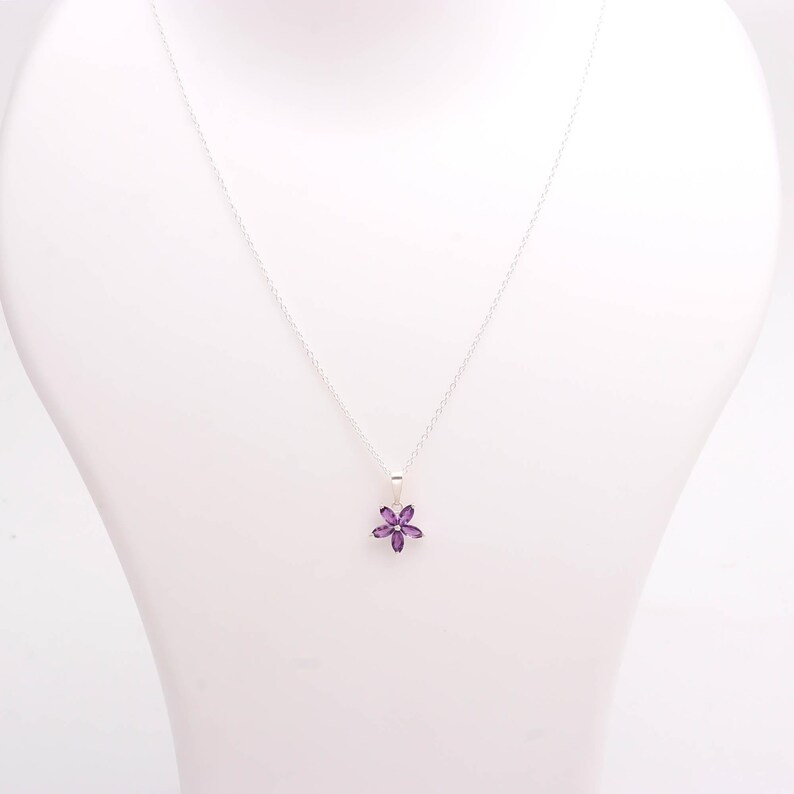 May include: A silver necklace with a small, purple flower pendant. The pendant is a six-petal flower made of small, purple gemstones. The necklace is displayed on a white mannequin.