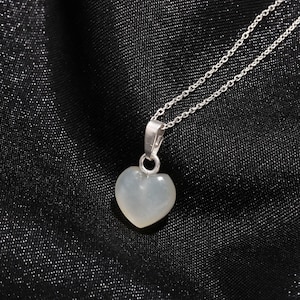May include: A silver necklace with a heart-shaped pendant. The pendant is a pale, translucent color, and the chain is delicate. The necklace is displayed against a black background.