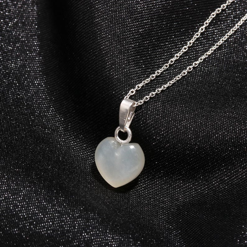 May include: A silver necklace with a heart-shaped pendant. The pendant is a pale, translucent color, and the chain is delicate. The necklace is displayed against a black background.