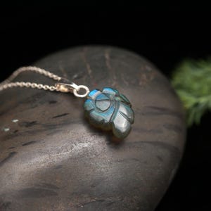 May include: A silver chain necklace with a carved labradorite pendant in the shape of a leaf. The pendant has a blue and green iridescent sheen.
