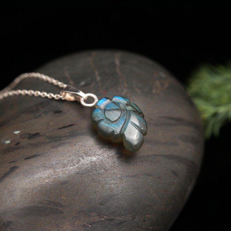 May include: A silver chain necklace with a carved labradorite pendant in the shape of a leaf. The pendant has a blue and green iridescent sheen.