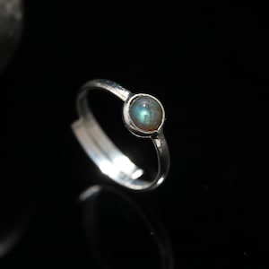 May include: A silver ring featuring a round, iridescent blue-green gemstone.