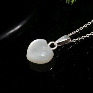 May include: A heart-shaped pendant necklace with a silver chain. The pendant is a pale, translucent color, and the chain is made of small, linked silver pieces. The necklace is displayed against a black background.