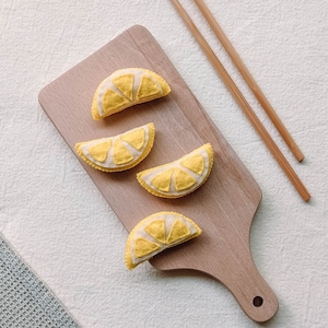 May include: Four felt lemon slices on a wooden cutting board with a pair of wooden chopsticks.