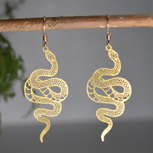 May include: A pair of gold-tone snake earrings. The earrings are made of metal and feature a detailed snake design. The snakes are curled up and have a textured surface.