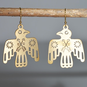 May include: A pair of gold-tone earrings featuring a cutout design of a stylized bird with arrows and sun symbols.
