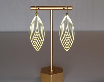 Puede incluir: Un par de pendientes de color dorado con un diseño geométrico en forma de hoja. Los pendientes se muestran en un soporte dorado.