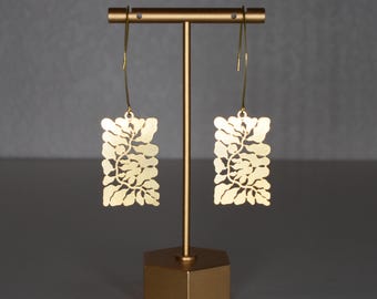 May include: Gold earrings with a delicate, leafy design. The earrings are hanging from a gold stand.