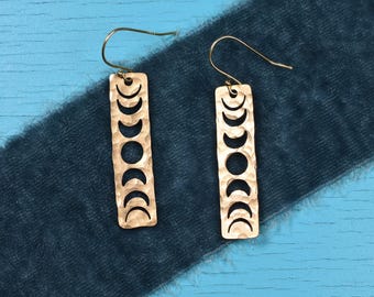 Könnte beinhalten: Ein Paar goldfarbene Ohrringe mit gehämmerter Textur. Jeder Ohrring hat eine rechteckige Form mit einem ausgeschnittenen Design aus acht Mondsicheln.