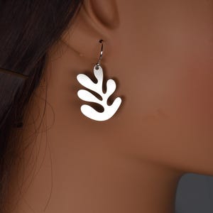 Puede incluir: Un pendiente plateado con forma de hoja estilizada. El pendiente est&aacute; suspendido de un peque&ntilde;o gancho y se lleva en la oreja. El dise&ntilde;o presenta una serie de formas redondeadas y abstractas.