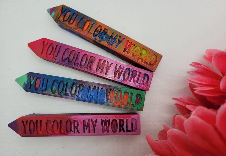 Pu&ograve; includere: Quattro pastelli colorati con il testo "YOU COLOR MY WORLD" stampato su ciascuno. I pastelli sono disposti verticalmente, con il pastello superiore che &egrave; arancione e giallo, il secondo pastello che &egrave; rosa e viola, il terzo pastello che &egrave; blu e verde, e il pastello inferiore che &egrave; rosso e viola.