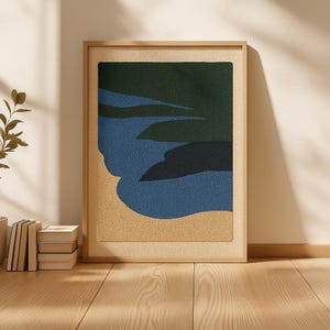 Könnte beinhalten: Ein gerahmtes abstraktes Kunstwerk mit strukturiertem Design. Das Kunstwerk zeigt eine Landschaft mit einem dunkelgrünen oberen Bereich, blauem Wasser und einem beigefarbenen unteren Bereich. Der Rahmen besteht aus hellem Holz und verleiht dem Stück eine natürliche Note.