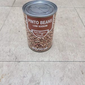 May include: A can of pinto beans with a brown label that reads "Pinto Beans Low Sodium". The can is labeled "Michigan Made" and contains 15 oz (425 grams) of beans.