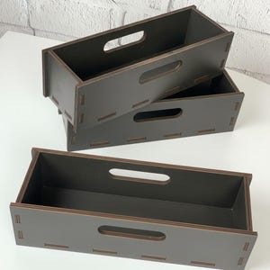May include: Three stacked, dark brown wooden storage boxes with rectangular shapes and handle cutouts. The boxes are made of wood and have a simple, modern design. The boxes are empty and ready to be filled.