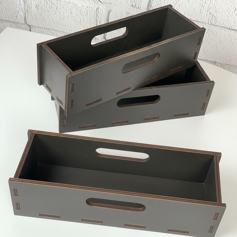 May include: Three stacked, dark brown wooden storage boxes with rectangular shapes and handle cutouts. The boxes are made of wood and have a simple, modern design. The boxes are empty and ready to be filled.