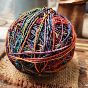 Peut inclure: Une pelote de ficelle sphérique composée de brins multicolores dans des tons orange, rouge foncé, violet, bleu sarcelle et bleu marine. La ficelle a un aspect texturé et fibreux, enroulée en une forme dense et irrégulière.