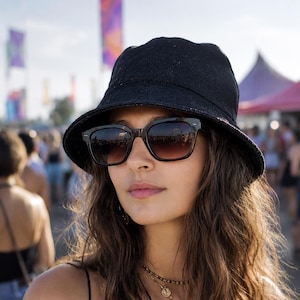 May include: A person wearing a black bucket hat and dark-framed sunglasses. The sunglasses reflect a crowd of people and the sky. The person is also wearing a necklace with a pendant.