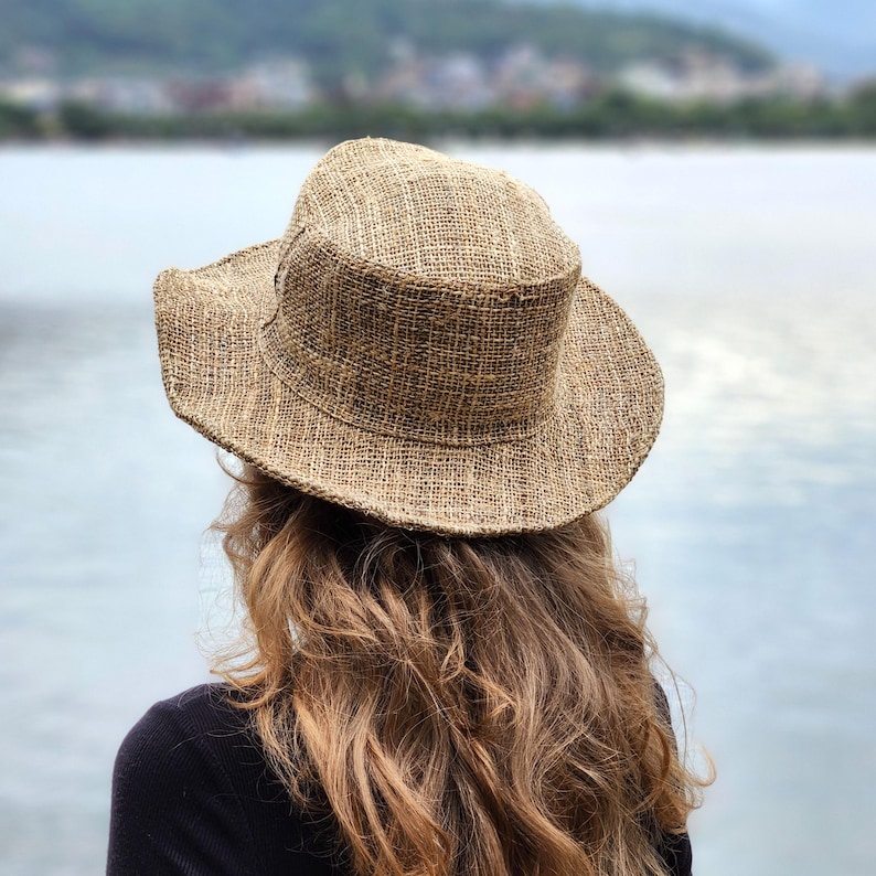 May include: A woven, wide-brimmed hat in shades of tan and brown. The hat has a structured crown and a slightly curved brim. The hat is made of a natural fiber material, and appears to be a sun hat or a casual hat.