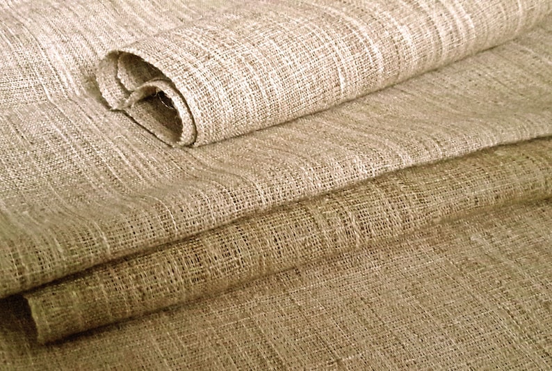 Może przedstawiać: Zbliżenie na stos naturalnego beżowego materiału lnianego. Materiał ma splecioną strukturę i lekko szorstkie wykończenie.
