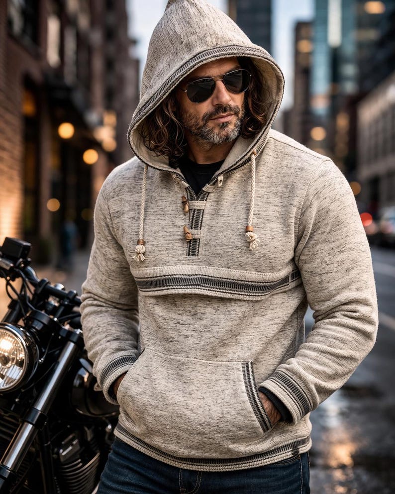 Op de afbeelding: Een lichtgrijze hoodie met een voorzak en houten knevelsluitingen. De hoodie heeft zwart-grijze gestreepte accenten en een capuchon met trekkoord. De persoon op de foto draagt een zonnebril en een blauwe spijkerbroek.