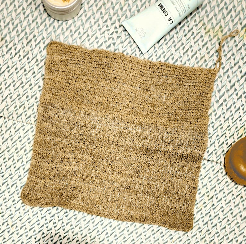 K&ouml;nnte beinhalten: Ein brauner, rechteckiger Bade-Schwamm aus gewebtem Material mit einem geknoteten Griff. Der Schwamm ist aus Naturfasern hergestellt und hat eine raue Textur.