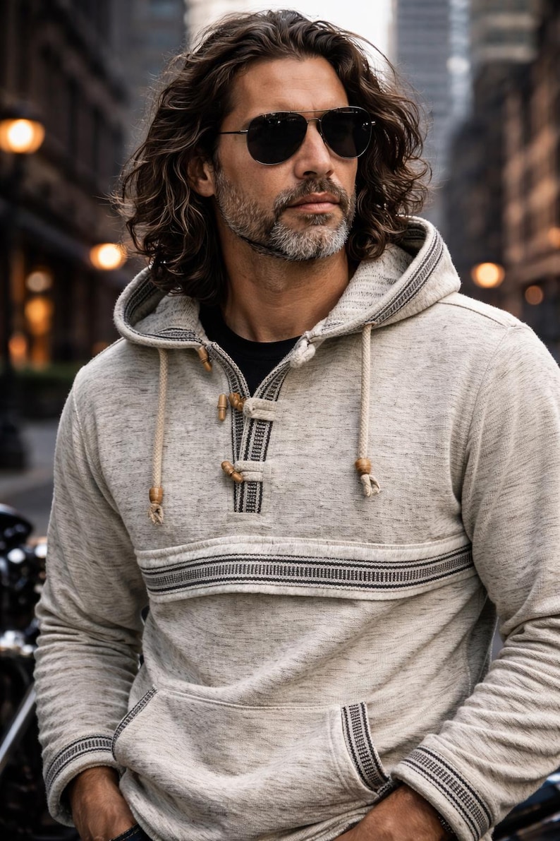 Op de afbeelding: Een lichtgrijze hoodie met een trekkoord en houten knevels. De sweatshirt heeft een horizontale streep over de borst en een voorzak. Het model draagt een zonnebril.