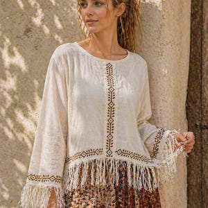 Könnte beinhalten: Cremefarbenes Langarm-Top mit brauner geometrischer Stickerei und Fransen. Das Top wird mit einem Rock mit Blumenmuster kombiniert. Das Outfit hat einen Bohemian-Stil.