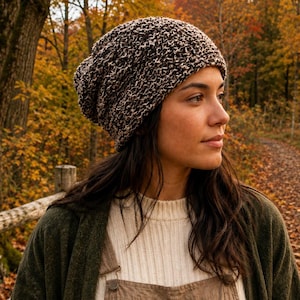 Peut inclure: Un bonnet en tricot affaissé présentant un motif texturé et chiné dans des tons brun foncé et crème. Le bonnet a une forme arrondie et décontractée avec une construction tissée épaisse qui offre un aspect dense, couvrant le haut de la tête.