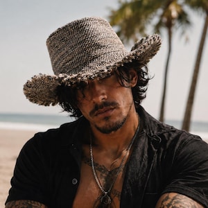 May include: A textured, woven fedora hat in shades of brown and gray, featuring a structured crown and a wide, frayed-edge brim. The hat is crafted from a dense, multi-tonal material that creates a mottled appearance across the entire surface.
