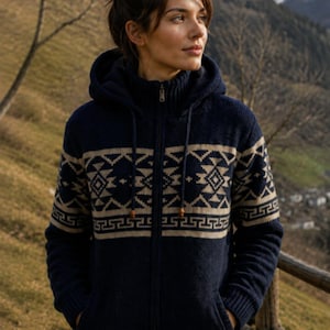 Peut inclure: Un gilet à capuche zippé bleu marine avec un motif géométrique beige sur la poitrine et les manches. Ce vêtement en tricot présente un col montant, une fermeture éclair intégrale, des poignets et un ourlet côtelés, ainsi que deux poches.