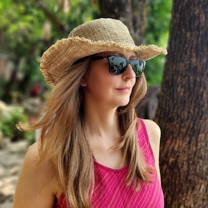May include: A straw hat with a frayed brim and black sunglasses. The hat is a light tan color. The sunglasses have a black frame. The person is wearing a pink tank top.