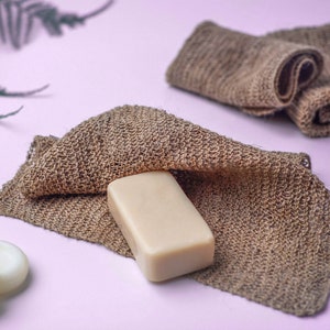 K&ouml;nnte beinhalten: Ein St&uuml;ck Seife liegt auf einem braunen gewebten Tuch. Das Tuch ist &uuml;ber die Seife gefaltet und die R&auml;nder des Tuches sind sichtbar. Die Seife ist hellbeige und rechteckig. Der Hintergrund ist hellrosa.