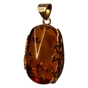 Puede incluir: Un colgante de oro con una piedra de ámbar grande engastada en un delicado diseño floral.