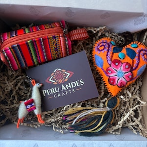 May include: A gift box containing a small orange striped zippered pouch, a white felt llama keychain, a dark brown card with the text PERU ANDES CRAFTS, and an orange heart-shaped felt ornament with floral embroidery and a multi-colored yarn tassel.