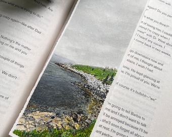 Peut inclure: Peinture de paysage d'un rivage rocheux avec de l'herbe verte et un plan d'eau. L'œuvre d'art est sur un morceau de papier rectangulaire, placé dans les pages d'un livre ouvert.