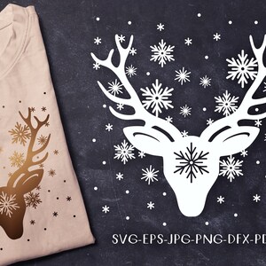 May include: A white silhouette of a reindeer with antlers, surrounded by snowflakes. The reindeer is on a dark background with the text "SVG-EPS-JPG-PNG-DFX-PDF" at the bottom.