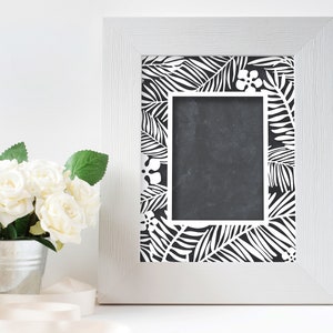 Pu&ograve; includere: Una cornice bianca con un design a foglie tropicali in bianco e nero. La cornice &egrave; vuota e pronta per una foto.