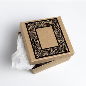 Pu&ograve; includere: Una scatola regalo di cartone marrone con un design nero di foglie e fiori tropicali sul coperchio. La scatola &egrave; aperta e l'interno &egrave; rivestito di carta velina bianca.