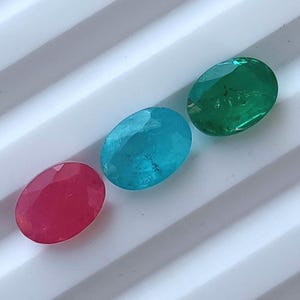 Puede incluir: Tres piedras preciosas de forma ovalada: un rubí rojo, una aguamarina azul verdosa y una esmeralda verde.
