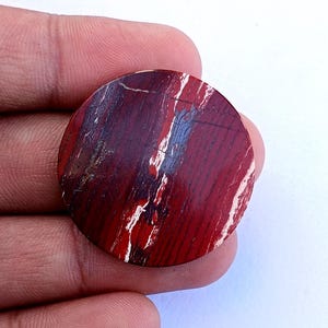 以下が含まれることがあります： 深紅、黒、白の縞模様が印象的な、丸く磨かれた石。石の表面は滑らかで光沢があり、円形がはっきりと定義されています。色と質感の自然なバリエーションが、ユニークな外観を作り出しています。